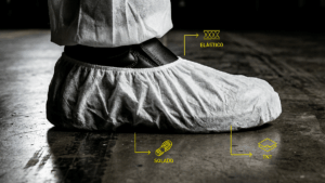 Grande plano lateral de um propé de TNT branco com ícones amarelos a indicar o elástico, o tecido e o solado antiderrapante.