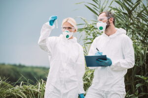 cientista masculino em traje de proteção e máscara escrevendo na prancheta enquanto sua colega examinava