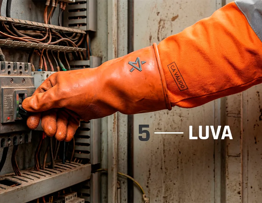 Close-up de luva isolante el&eacute;trica laranja da Astro Distribuidora acionando disjuntor industrial. Carimbo de CA V&Aacute;LIDO em destaque. Legenda 5 - LUVA.