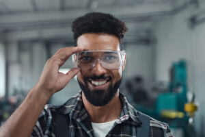Retrato de um jovem trabalhador industrial feliz atuando em uma oficina metalúrgica, em ambiente interno, olhando para a câmera.
