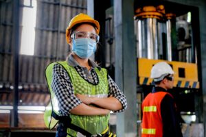 Operária ou técnica de fábrica, usando máscara higiênica, demonstra confiança ao lado de seu colega engenheiro no local de trabalho, em meio às preocupações com o impacto da pandemia de coronavírus na indústria.