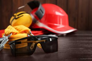 Óculos de proteção pretos e equipamentos de segurança desfocados ao fundo.